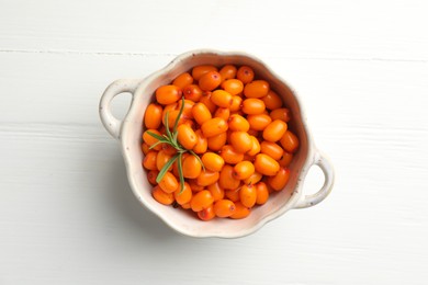 Photo of Fresh sea buckthorn berries in dish and leaves on white wooden table, top view