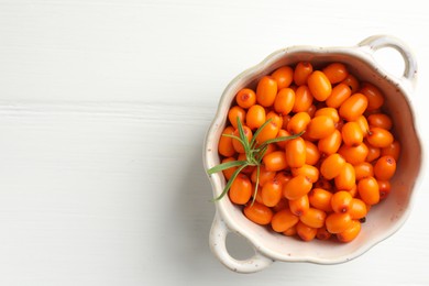 Photo of Fresh sea buckthorn berries in dish and leaves on white wooden table, top view. Space for text