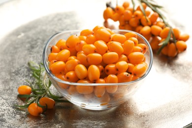 Photo of Fresh sea buckthorn berries in bowl and leaves on grey table, closeup