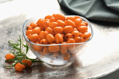 Photo of Fresh sea buckthorn berries in bowl and leaves on grey table, closeup