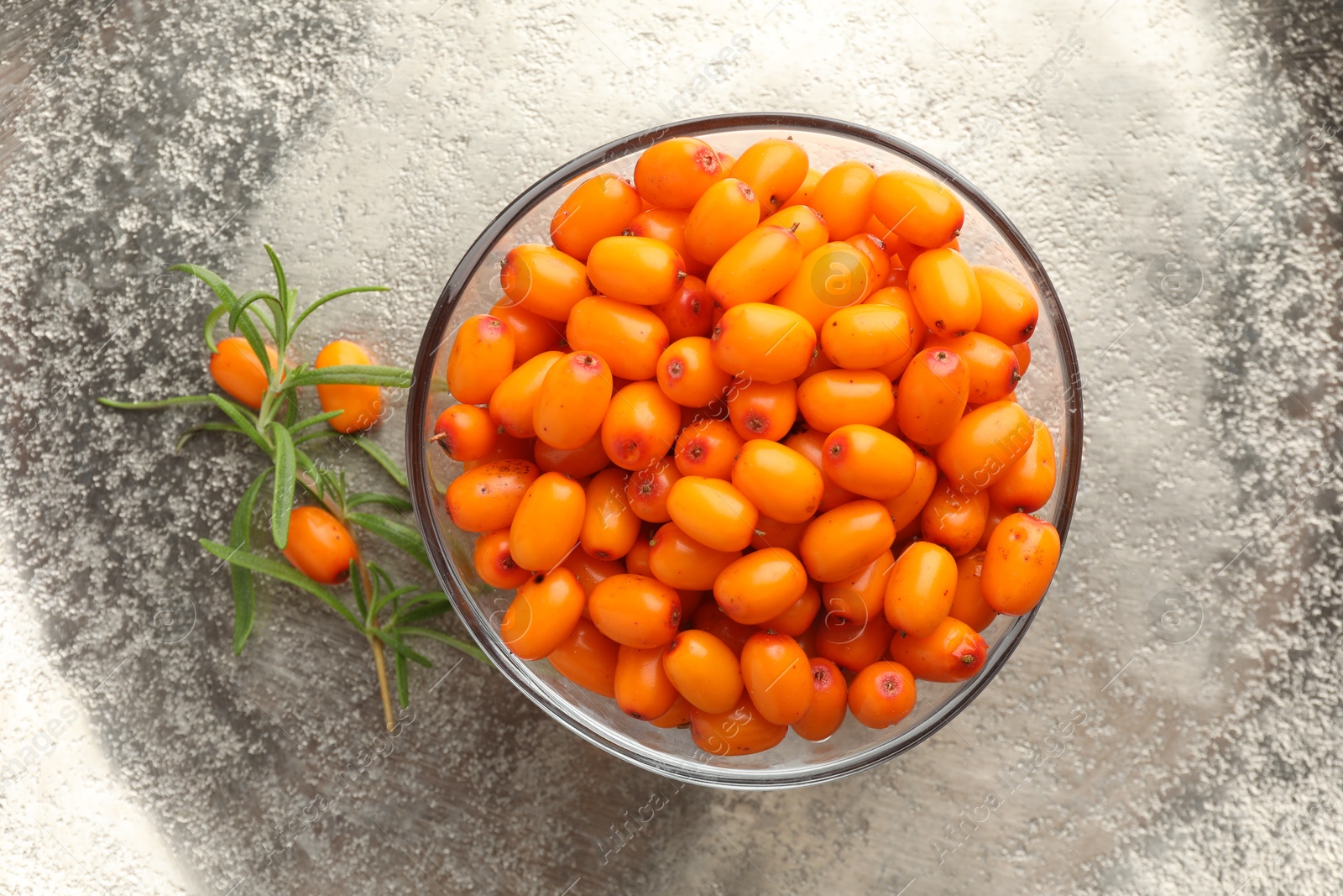 Photo of Fresh sea buckthorn berries in bowl and leaves on grey table, top view