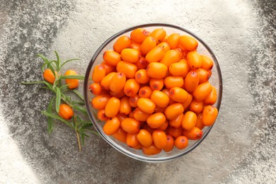 Photo of Fresh sea buckthorn berries in bowl and leaves on grey table, top view