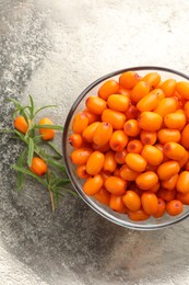 Photo of Fresh sea buckthorn berries in bowl and leaves on grey table, top view