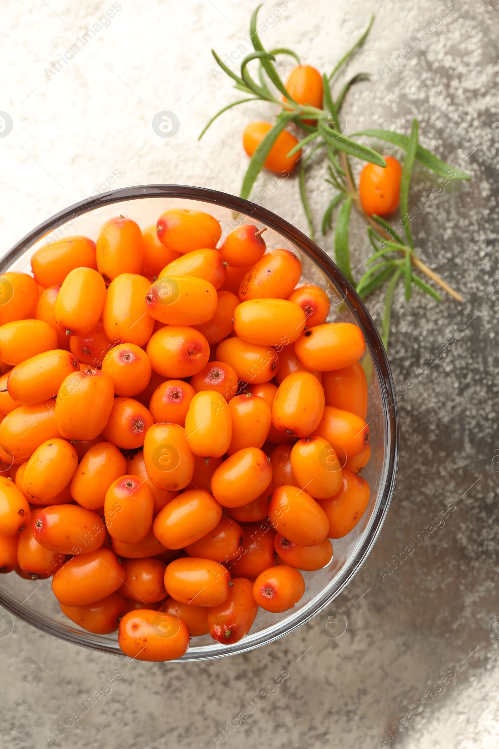 Photo of Fresh sea buckthorn berries in bowl and leaves on grey table, top view