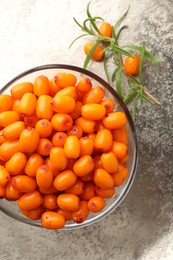 Photo of Fresh sea buckthorn berries in bowl and leaves on grey table, top view
