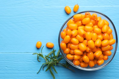 Photo of Fresh sea buckthorn berries in bowl and leaves on light blue wooden table, flat lay. Space for text