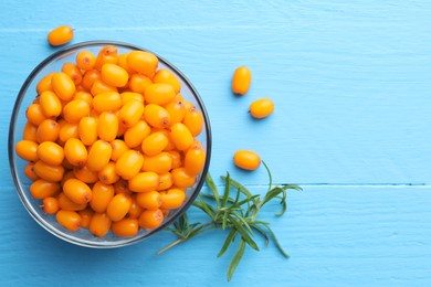 Photo of Fresh sea buckthorn berries in bowl and leaves on light blue wooden table, flat lay. Space for text