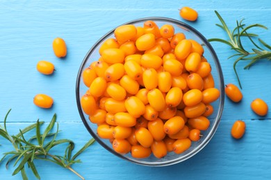 Photo of Fresh sea buckthorn berries in bowl and leaves on light blue wooden table, flat lay