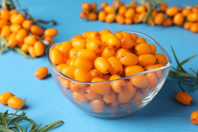 Photo of Fresh sea buckthorn berries in bowl and leaves on light blue wooden table, closeup