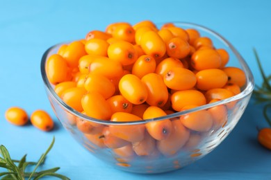 Photo of Fresh sea buckthorn berries in bowl and leaves on light blue wooden table, closeup