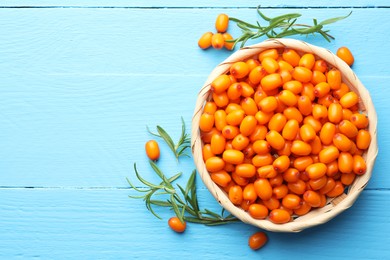Photo of Fresh sea buckthorn berries in wicker bowl and leaves on light blue wooden table, flat lay. Space for text
