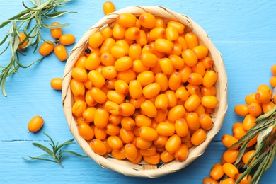 Photo of Fresh sea buckthorn berries in wicker bowl and leaves on light blue wooden table, flat lay