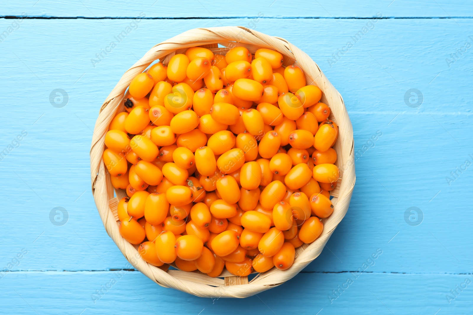 Photo of Fresh sea buckthorn berries in wicker bowl on light blue wooden table, closeup
