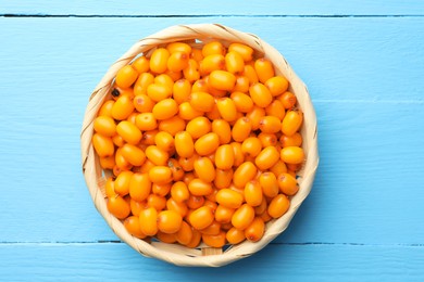 Photo of Fresh sea buckthorn berries in wicker bowl on light blue wooden table, closeup