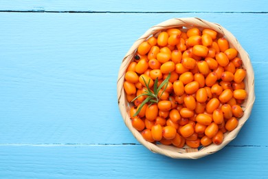 Photo of Fresh sea buckthorn berries in wicker bowl and leaves on light blue wooden table, top view. Space for text