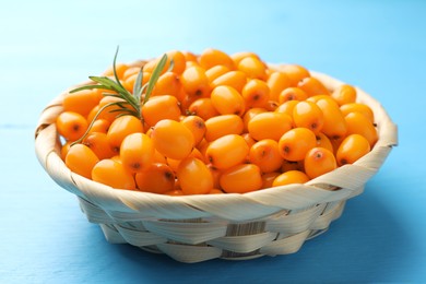 Photo of Fresh sea buckthorn berries in wicker bowl and leaves on light blue wooden table, closeup