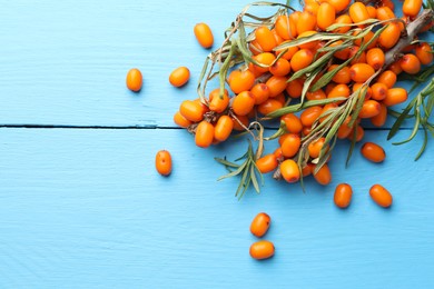 Photo of Fresh sea buckthorn berries and leaves on light blue wooden table, top view