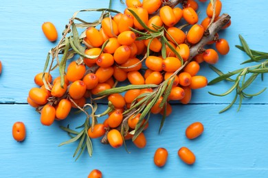 Photo of Fresh sea buckthorn berries and leaves on light blue wooden table, top view