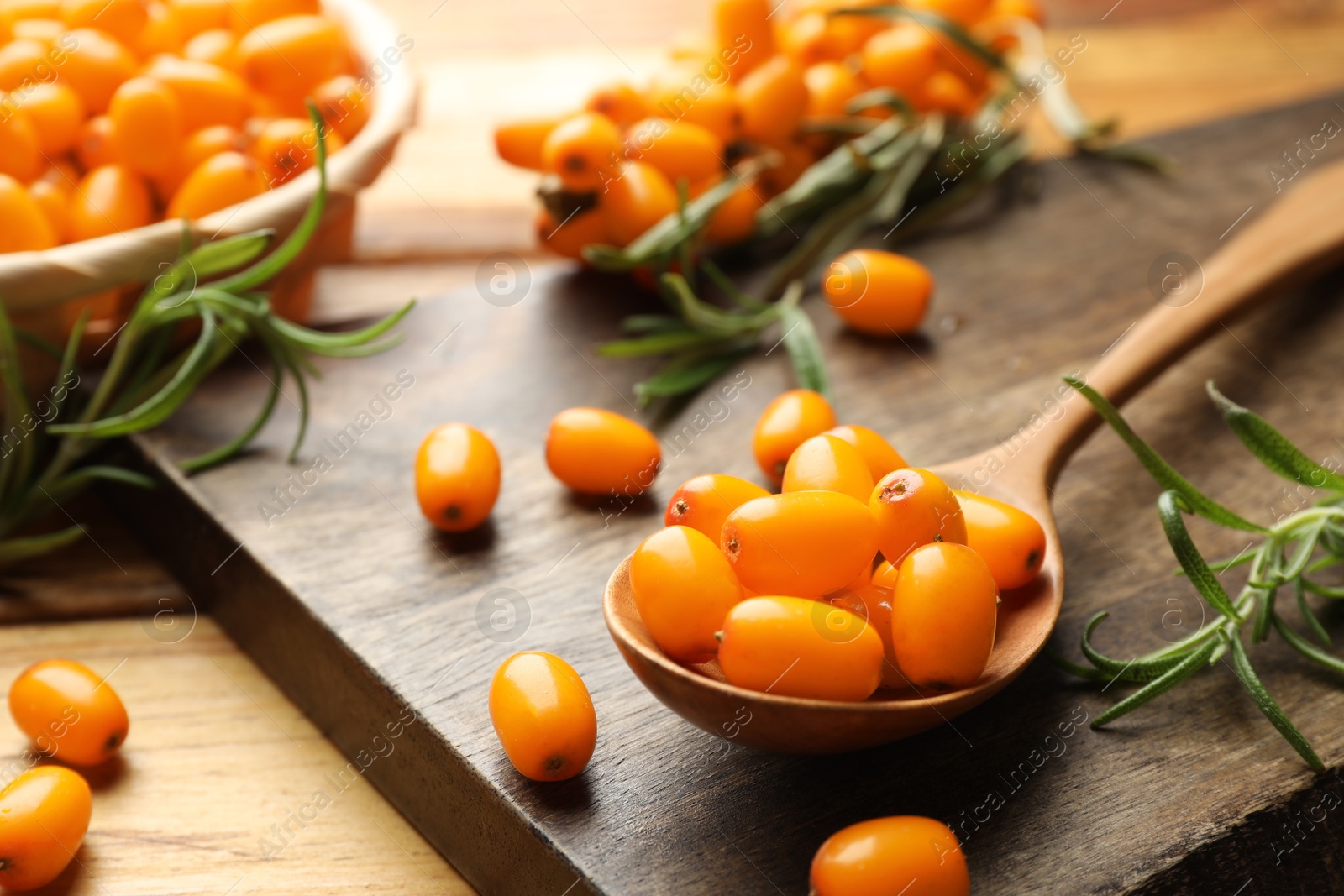 Photo of Fresh sea buckthorn berries, spoon and leaves on wooden table, closeup