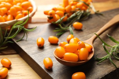 Photo of Fresh sea buckthorn berries, spoon and leaves on wooden table, closeup