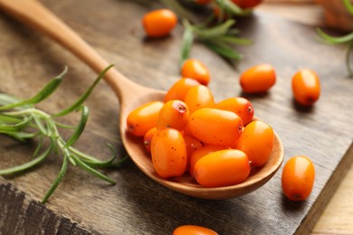 Photo of Fresh sea buckthorn berries, spoon and leaves on wooden table, closeup