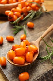 Photo of Fresh sea buckthorn berries, spoon and leaves on wooden table, closeup
