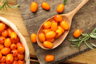 Photo of Fresh sea buckthorn berries, spoon and leaves on wooden table, flat lay
