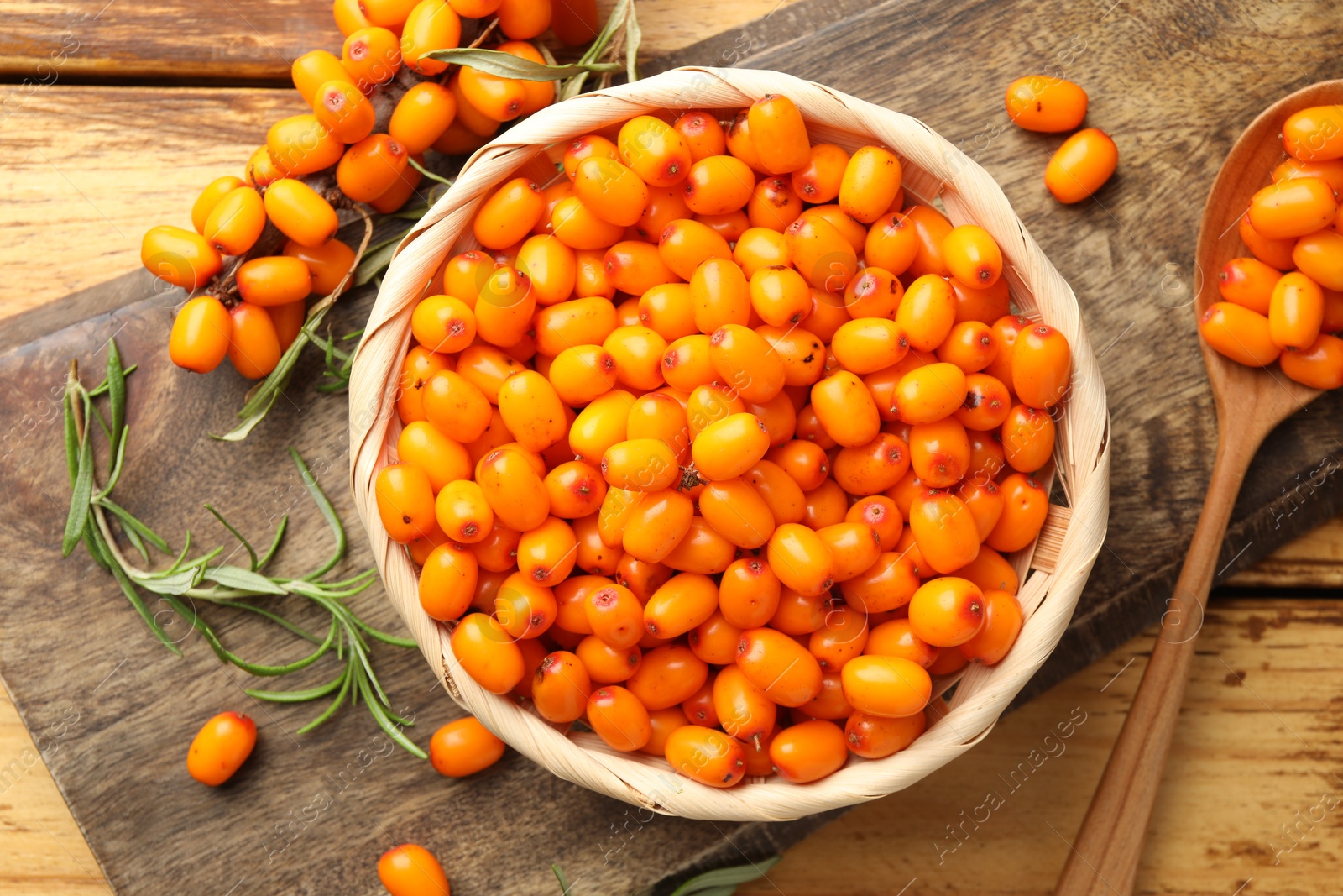 Photo of Fresh sea buckthorn berries in wicker bowl and leaves on wooden table, flat lay