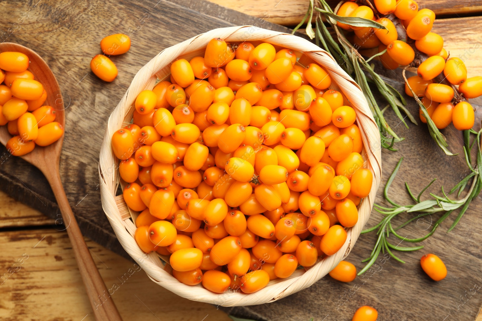 Photo of Fresh sea buckthorn berries in wicker bowl and leaves on wooden table, flat lay