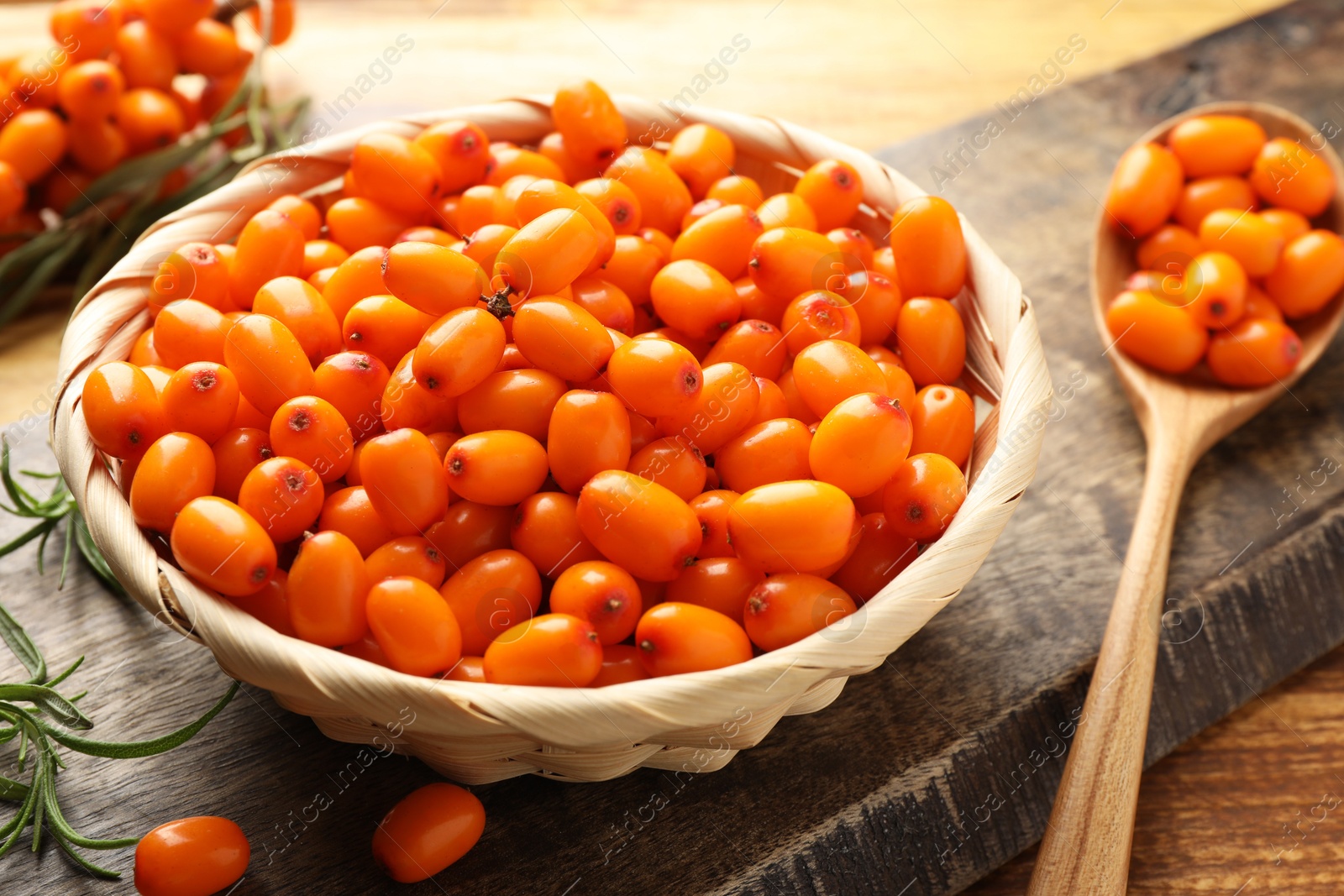 Photo of Fresh sea buckthorn berries in wicker bowl and leaves on wooden table, closeup