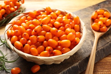 Photo of Fresh sea buckthorn berries in wicker bowl and leaves on wooden table, closeup