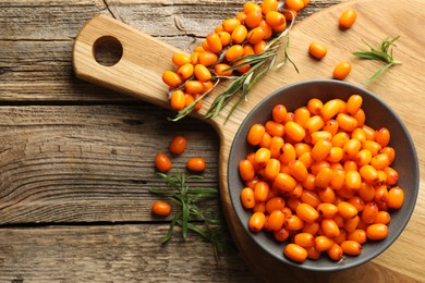 Photo of Fresh sea buckthorn berries in bowl and leaves on wooden table, flat lay