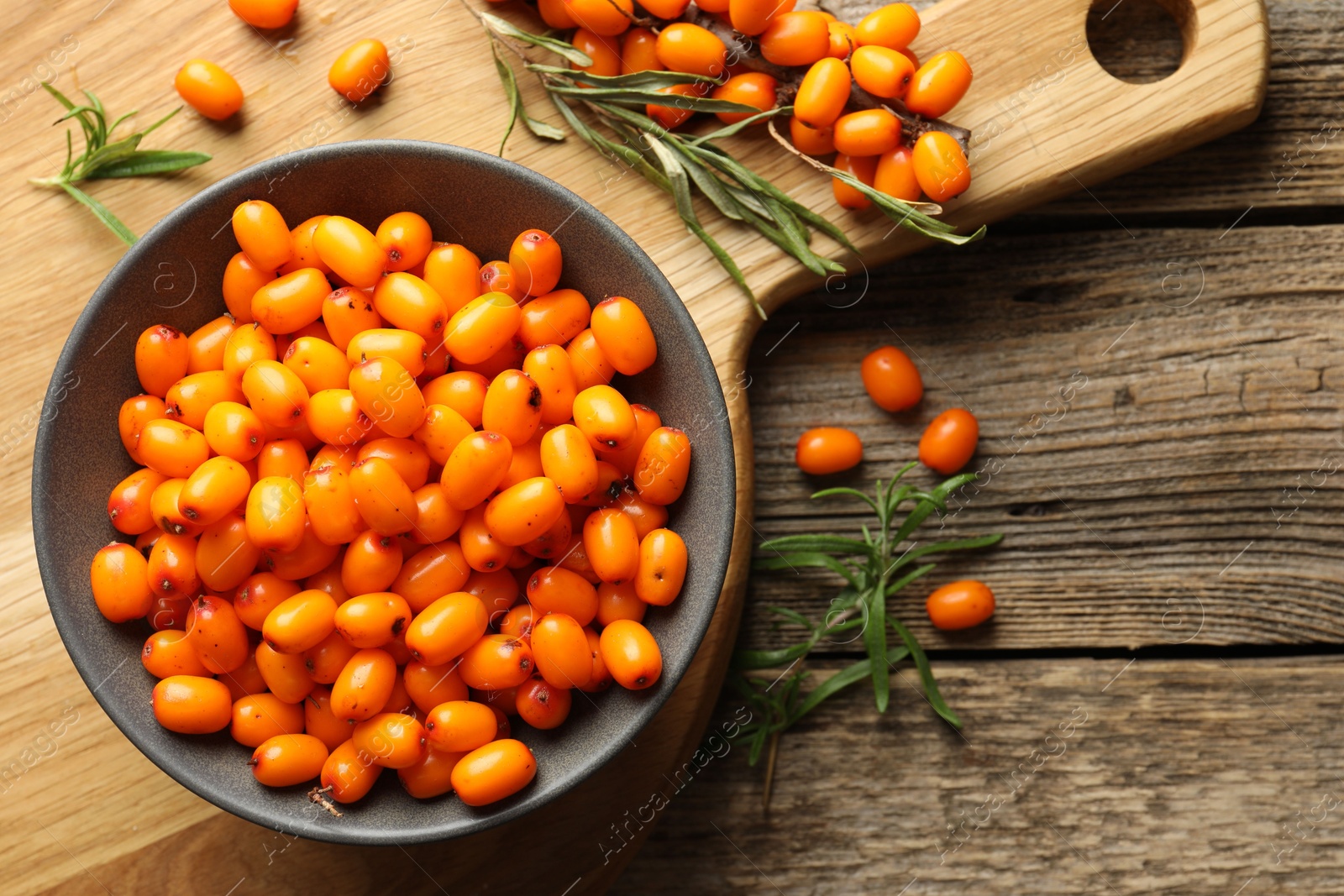 Photo of Fresh sea buckthorn berries in bowl and leaves on wooden table, flat lay