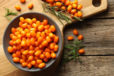 Photo of Fresh sea buckthorn berries in bowl and leaves on wooden table, flat lay