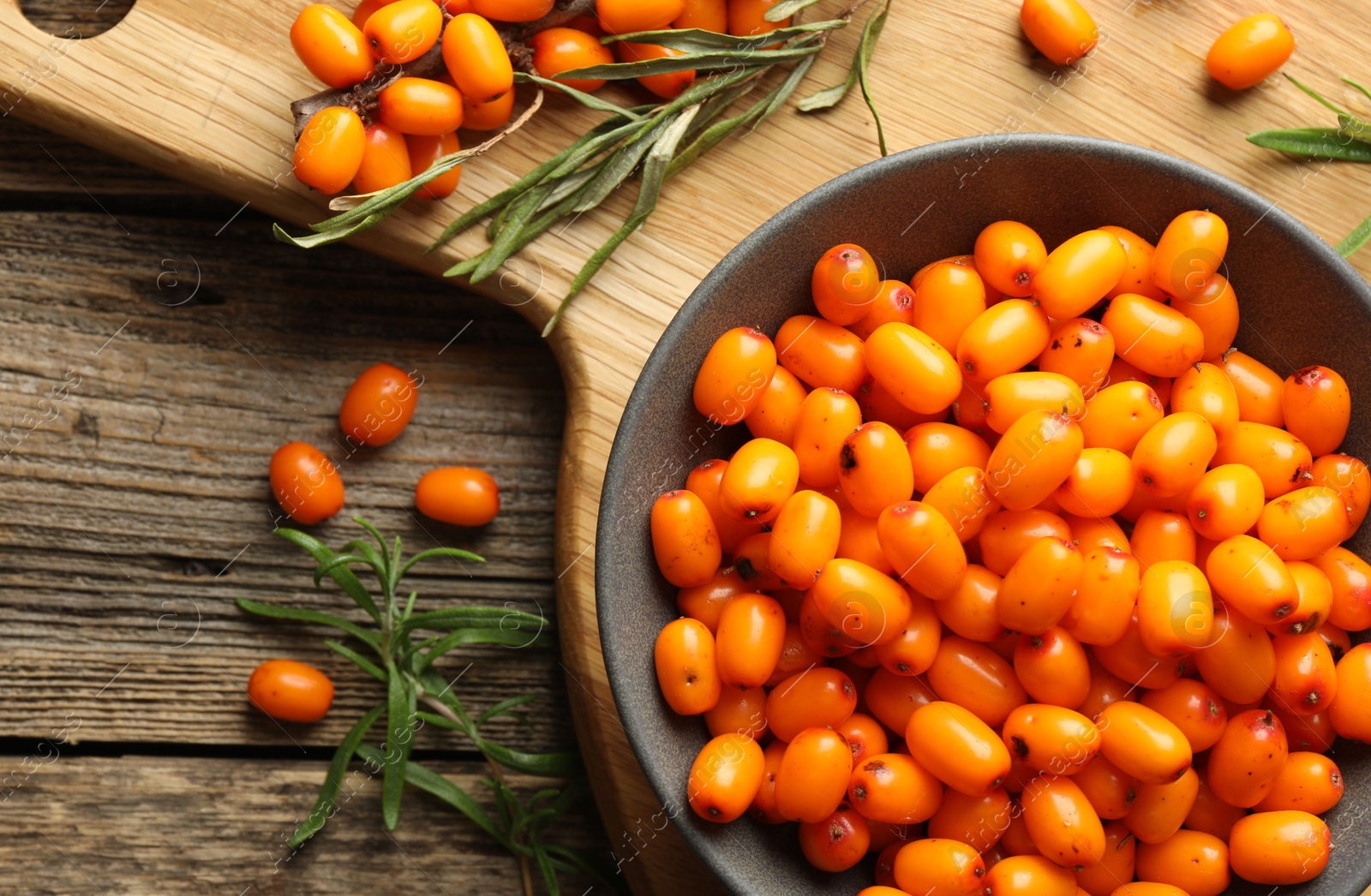 Photo of Fresh sea buckthorn berries in bowl and leaves on wooden table, flat lay