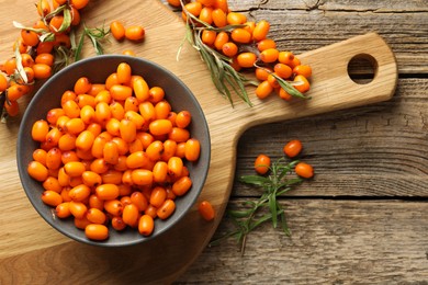 Photo of Fresh sea buckthorn berries in bowl and leaves on wooden table, flat lay