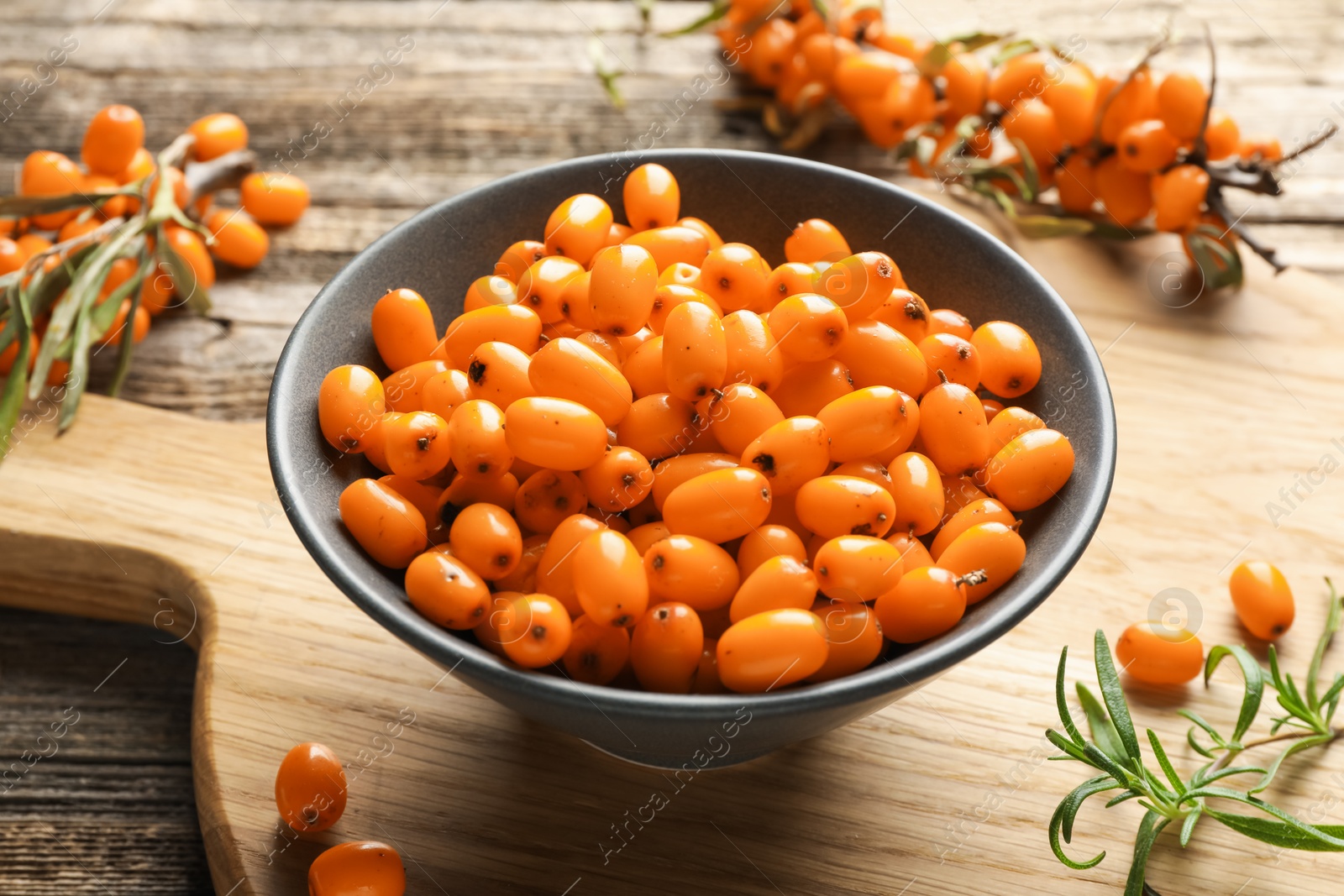 Photo of Fresh sea buckthorn berries in bowl and leaves on wooden table, closeup