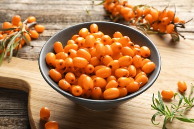 Photo of Fresh sea buckthorn berries in bowl and leaves on wooden table, closeup
