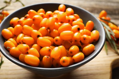 Photo of Fresh sea buckthorn berries in bowl on wooden table, closeup