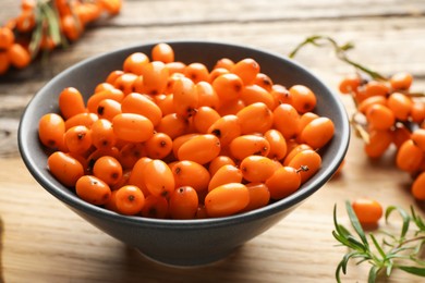 Photo of Fresh sea buckthorn berries in bowl and leaves on wooden table, closeup