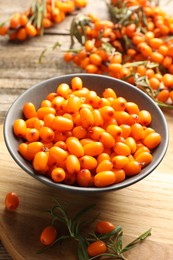 Photo of Fresh sea buckthorn berries in bowl and leaves on wooden table, closeup