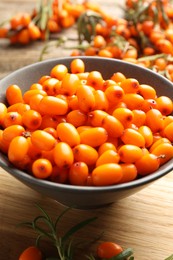 Photo of Fresh sea buckthorn berries in bowl and leaves on wooden table, closeup