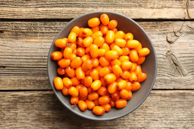 Photo of Fresh sea buckthorn berries in bowl on wooden table, top view