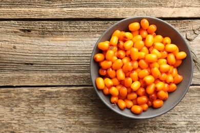 Photo of Fresh sea buckthorn berries in bowl on wooden table, top view. Space for text