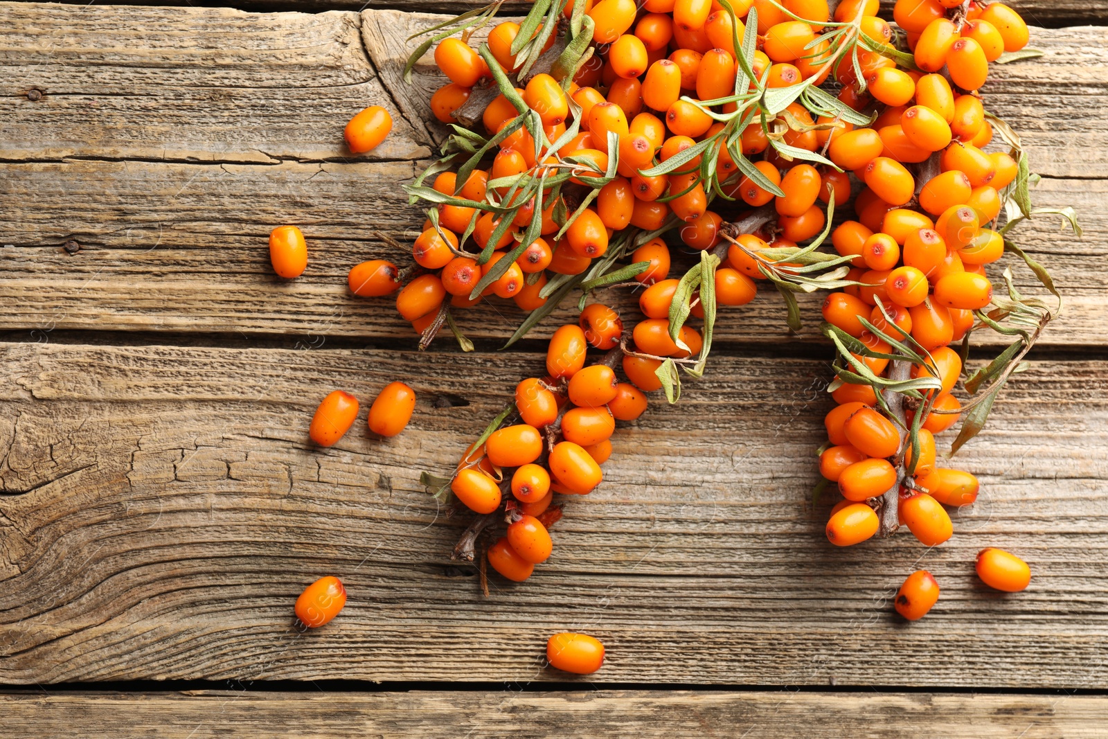Photo of Fresh sea buckthorn berries with leaves on wooden table, flat lay