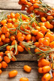 Photo of Fresh sea buckthorn berries with leaves on wooden table, closeup