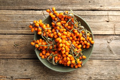 Photo of Fresh sea buckthorn berries with leaves in bowl on wooden table, top view