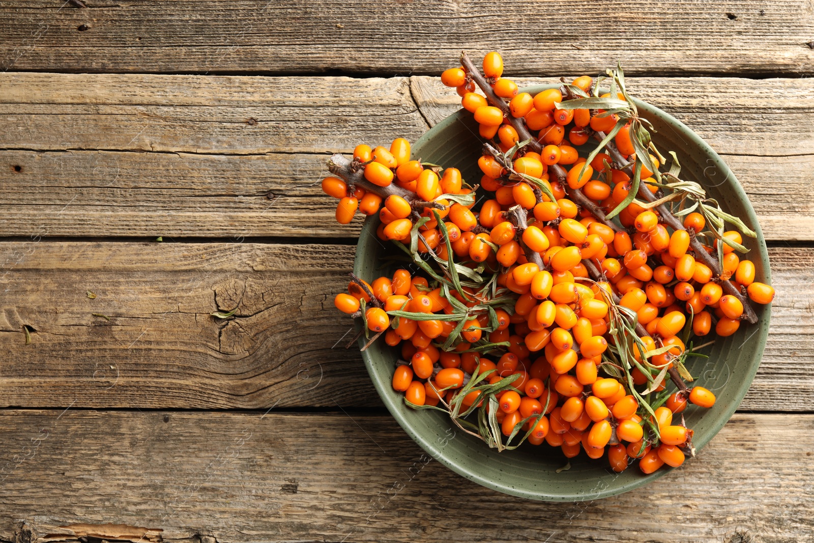 Photo of Fresh sea buckthorn berries with leaves in bowl on wooden table, top view. Space for text