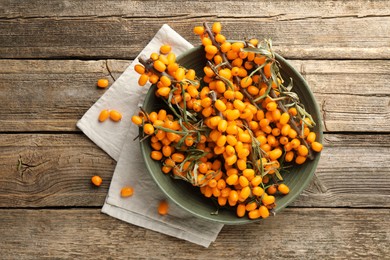Photo of Fresh sea buckthorn berries with leaves in bowl on wooden table, top view