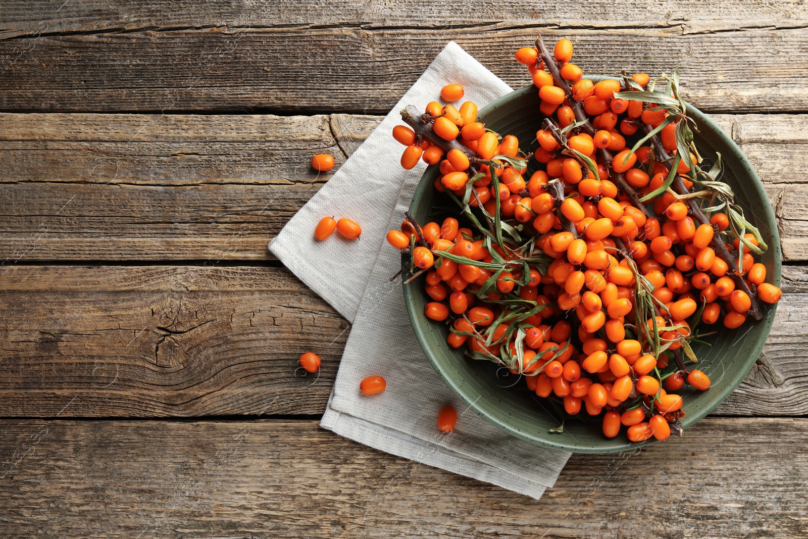 Photo of Fresh sea buckthorn berries with leaves in bowl on wooden table, top view. Space for text